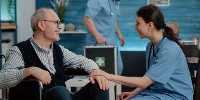 patient-with-physical-disease-getting-assistance-from-nurse-nursing-home-medical-assistant-talking-elder-man-sitting-wheelchair-about-healthcare-treatment-recovery-therapy-min